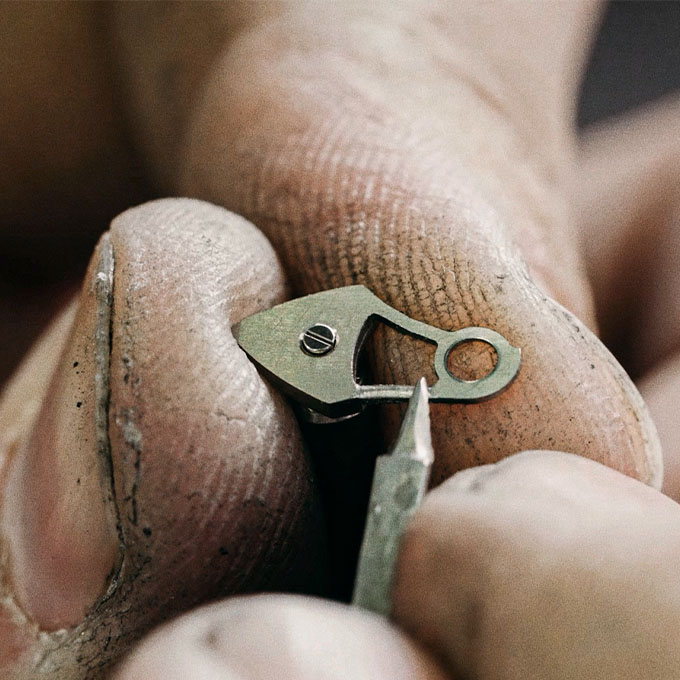 artisans working on a watch component with a file